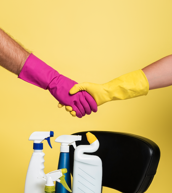 duas pessoas de luva rosa e amarela com um fundo amarelo dando as maos com produtos de limpeza profissional para empresa embaixo delas