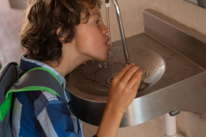 Vista lateral de um estudante caucasiano bebendo água da torneira no corredor da escola