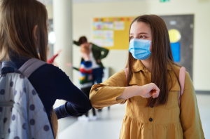 garotas em escolas com mascaras se cumprimentando com o ombro devido a pandemia de covid