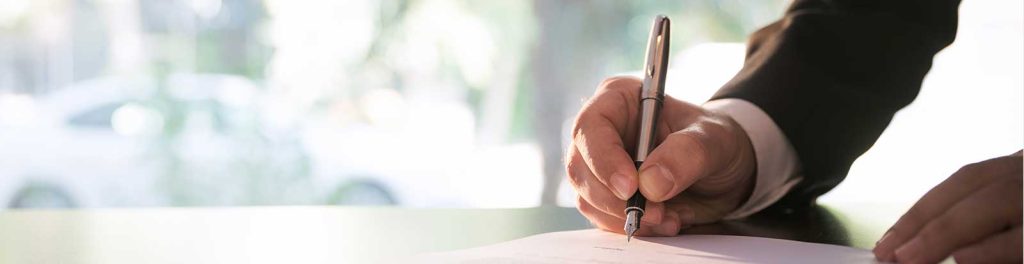 homem de terno assinando um documento close up com foco nas mãos dele segurando a caneta