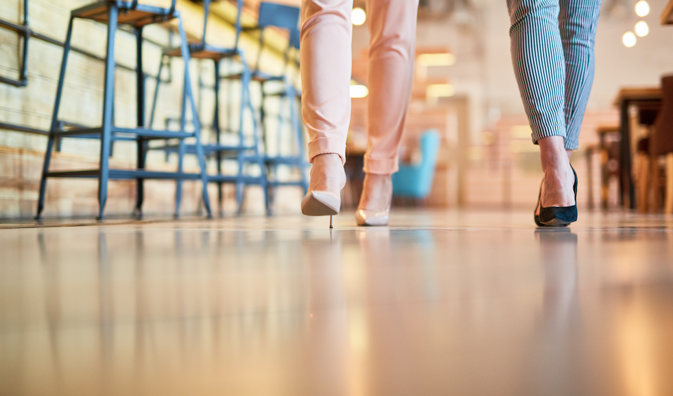 Duas jovens de leggins e sapatos de salto alto caminhando ao longo do balcão com cadeiras de bar com foco em um piso limpo após uma limpeza profissional de pisos em um restaurante