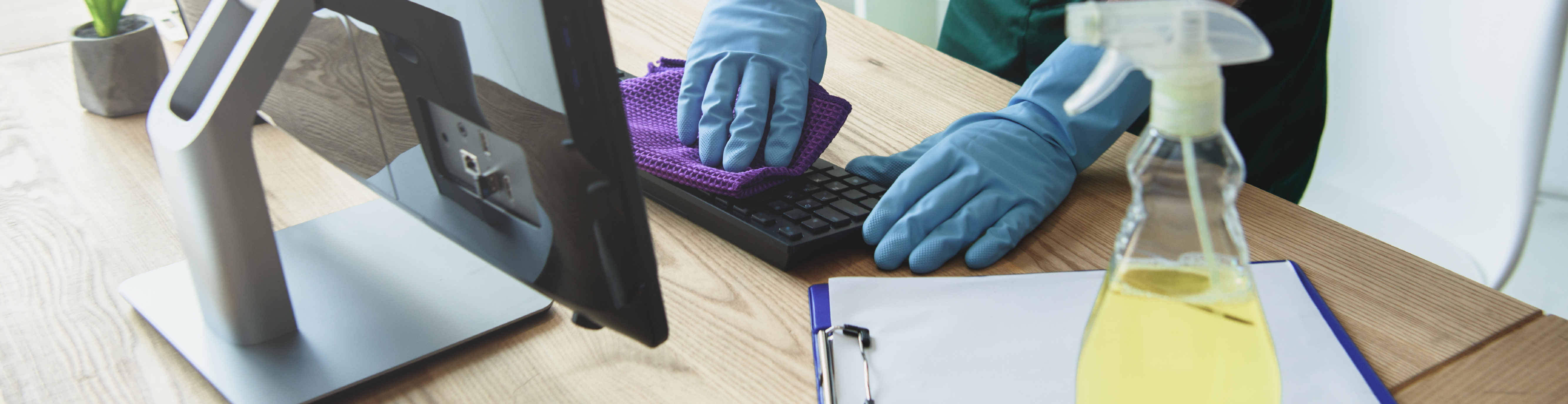 limpeza em escritórios sendo feita com operador limpando teclado de computador com luvas e pano de microfibra